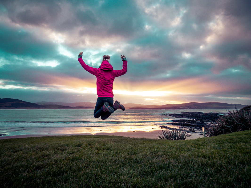 Woman jumping next to sea as the sun sets in the Catlins, South Island, New Zealand