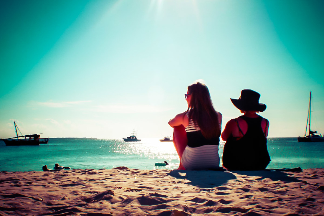 Picture of mother and daughter sitting in the sand overlooking the sea and ships
