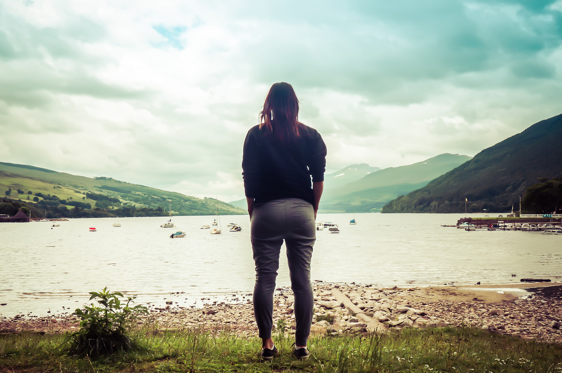 Picture of a woman standing in front of a lake looking at mountains and fields on a cloudy day