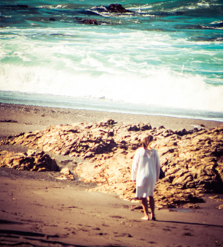 Picture of a girls standing on the beach in a white dress looking at the sea