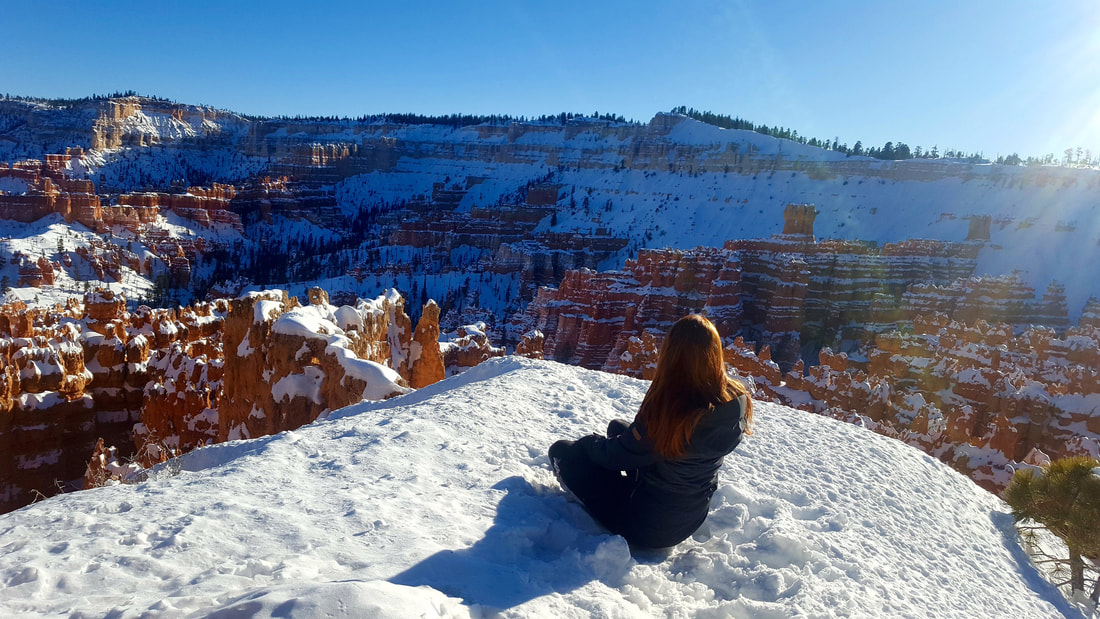 Picture of a girl sitting on a snowy mountain top overlooking other mountains covered in snow