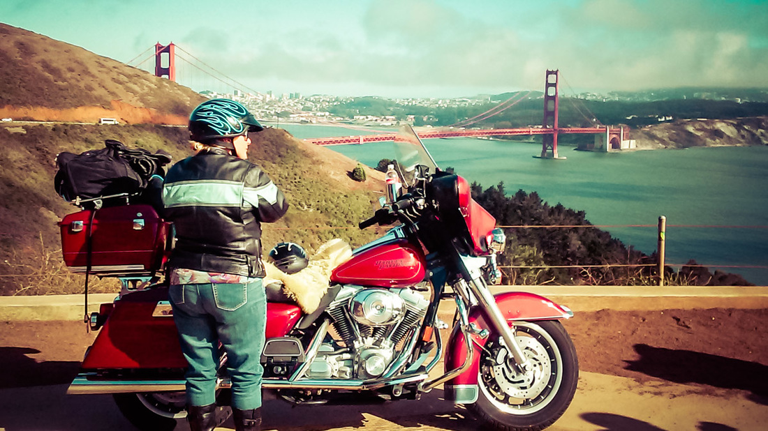 Picture of a woman standing in front of her motorbike overlooking the Golden Gate Bridge in San Francisco 