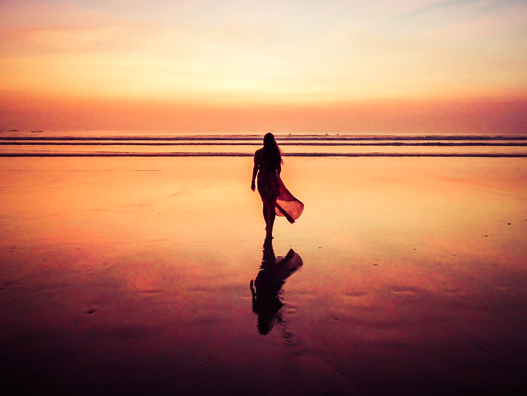 Picture of a woman walking along a beach at sunset 