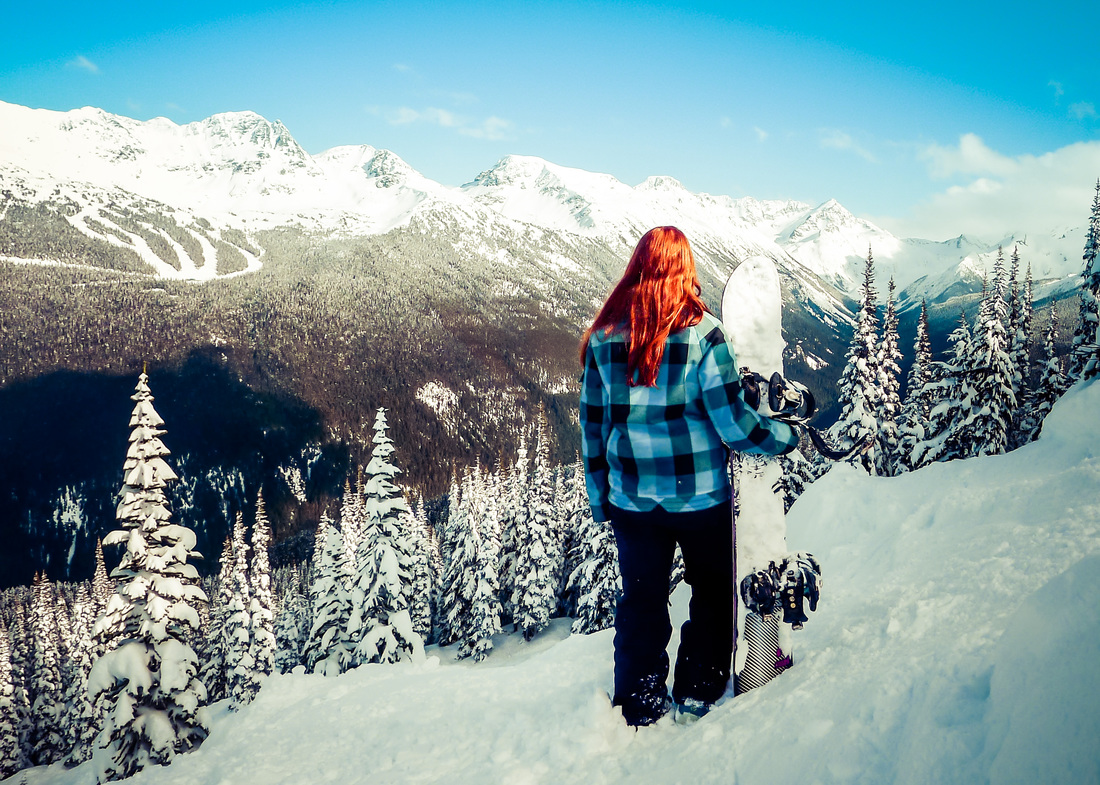 Picture of a woman holding her snowboard and overlooking snowy mountains in Canada 