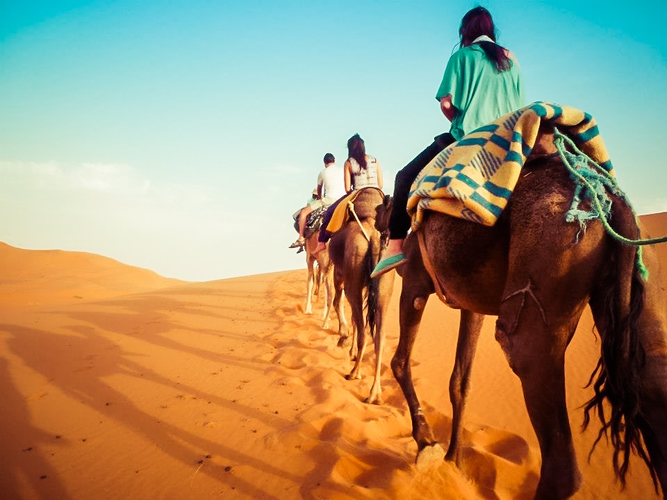 Picture of two women and one man riding on camels through the desert 