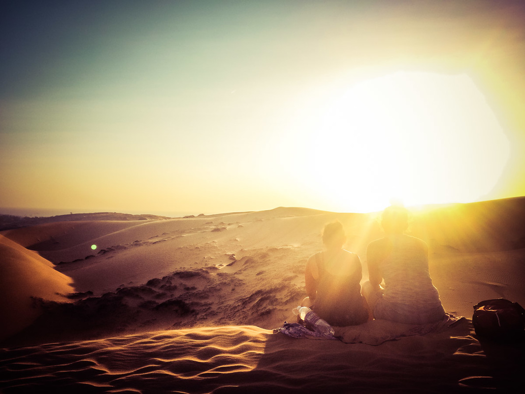 Picture of mother and daughter sitting next to each other in the desert sand overlooking the sand dunes at sunrise 