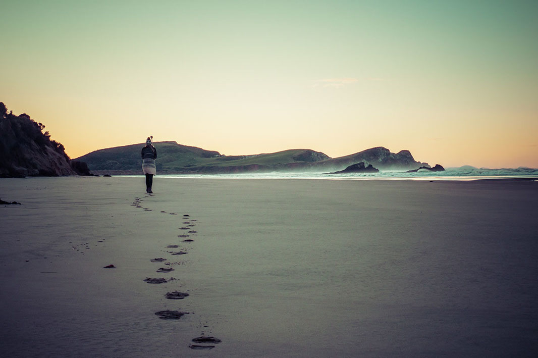Picture of a woman walking a long the beach at sunset in New Zealand