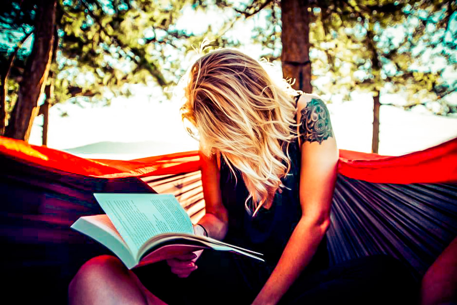 Picture of a woman sitting in a hammock surrounded by trees reading a book