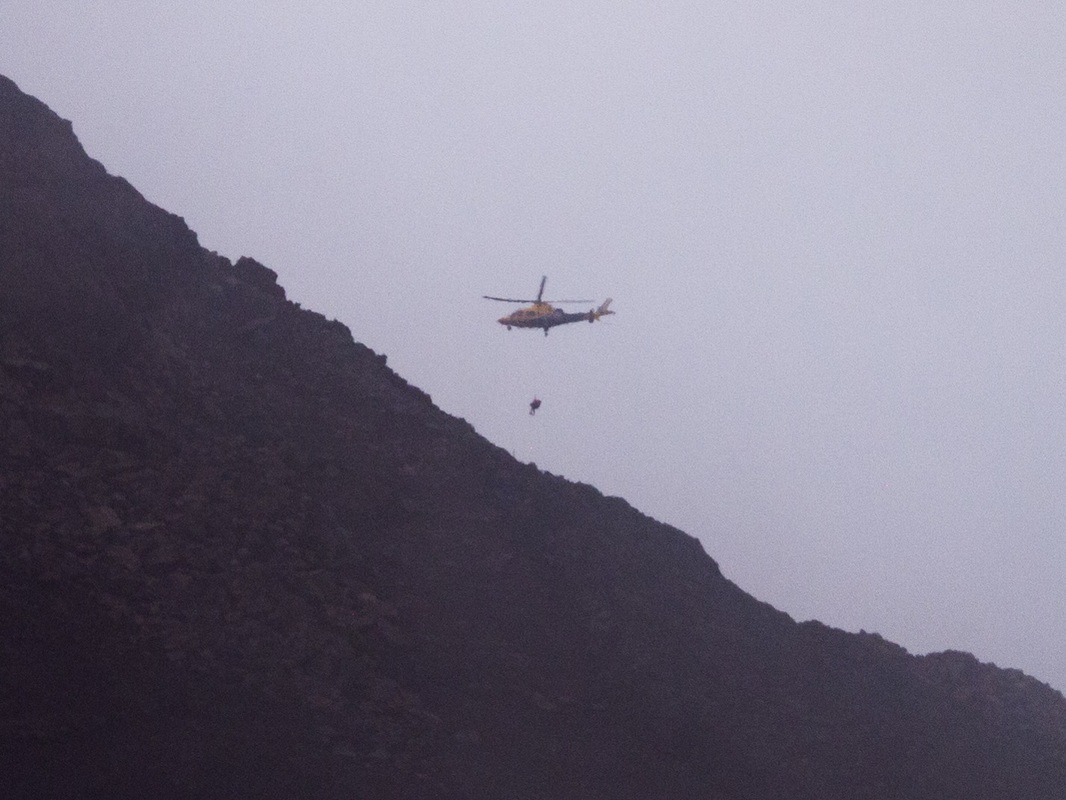 Picture of a helicopter rescuing someone from the top of  a mountain 