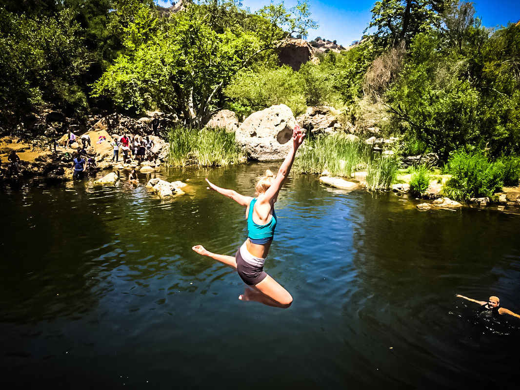 A woman jumps triumphantly into a wooded lake.