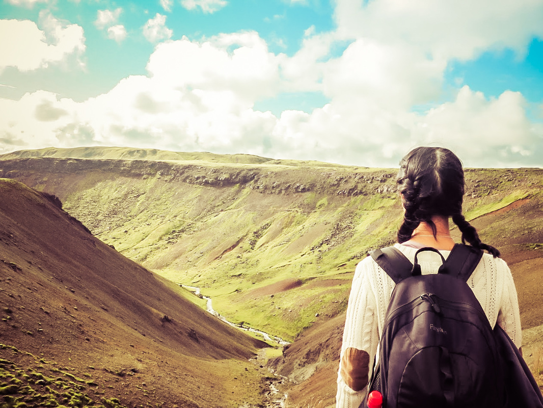 Picture of a woman standing at the top of a hill overlooking a river and mountains in Iceland