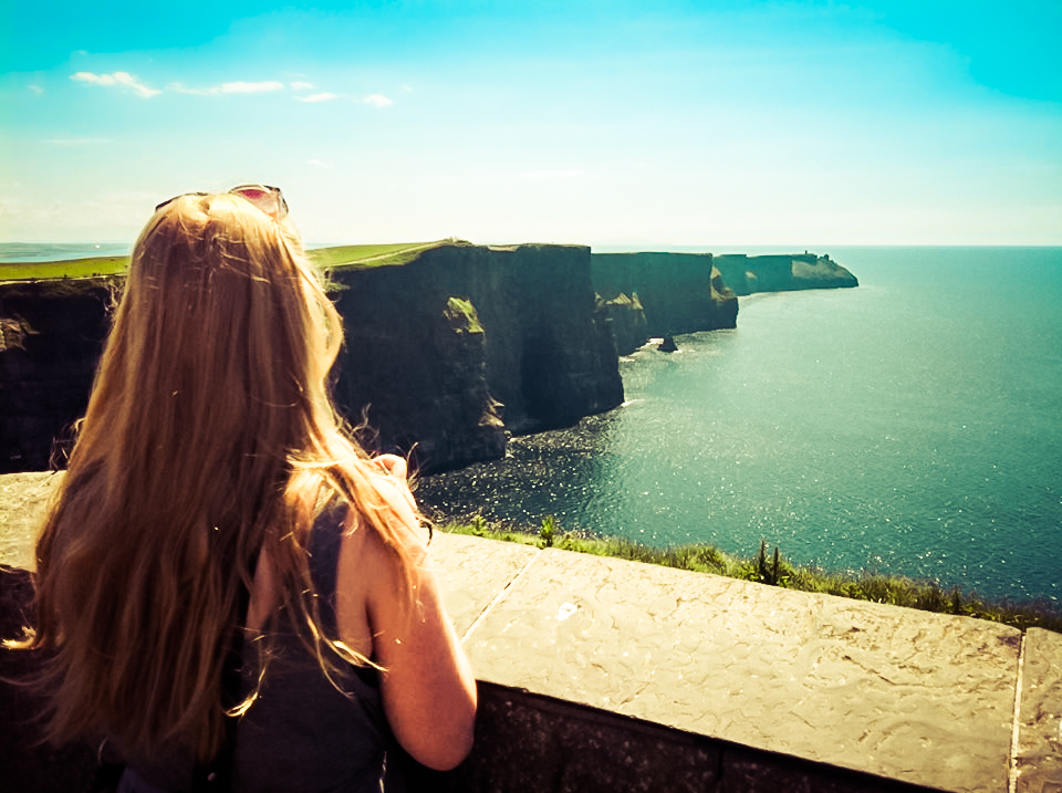 Picture of a woman overlooking the Cliffs of Moher in Ireland on a sunny day with blue skies
