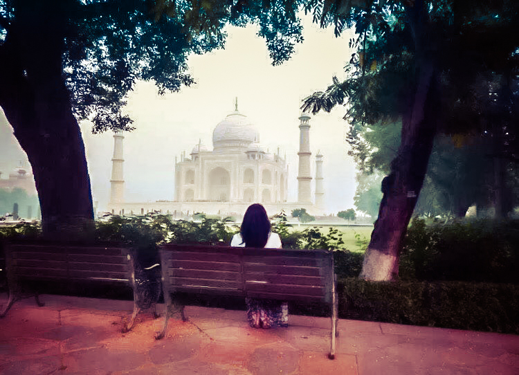 Picture of a woman sitting on a bench looking at the Taj Mahal in India 