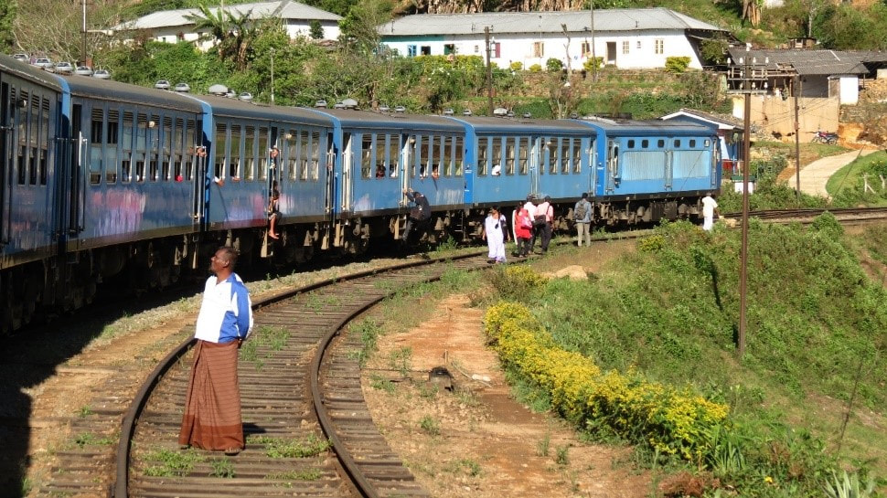 A train stops at a local train stations in Sri Lanka on the way from Kandy to Ella. A few passengers are jumping off the train while one man observes the scene