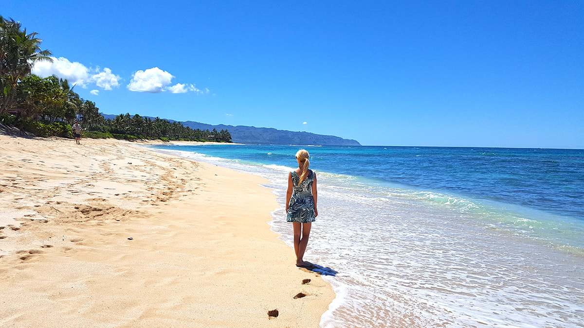 Woman walking along a beach in Hawaii looking at the ocean leaving footsteps in the sand