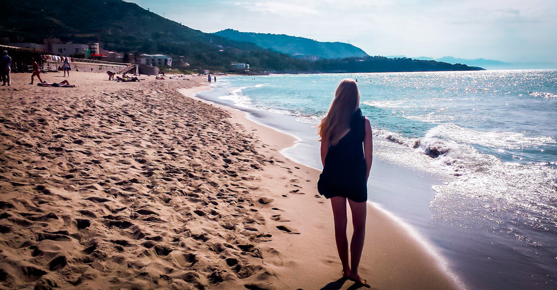 Woman walking pensively along an Italian beach in the sunshine