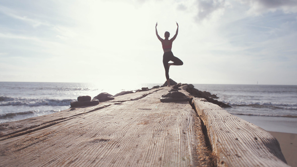 A woman does a yoga pose on a wooden pier in California