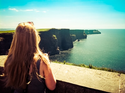 A woman overlooks the Cliffs of Moher in the sun, Ireland