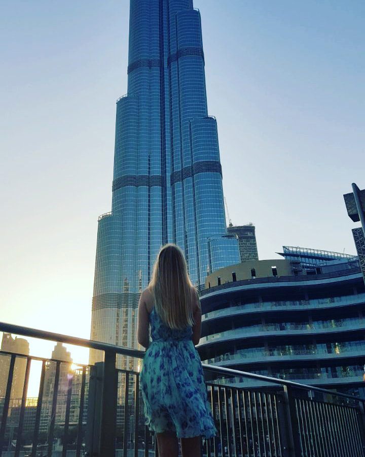 Picture of a woman standing in front of the Burj Khalifa in Dubai looking up towards the sky