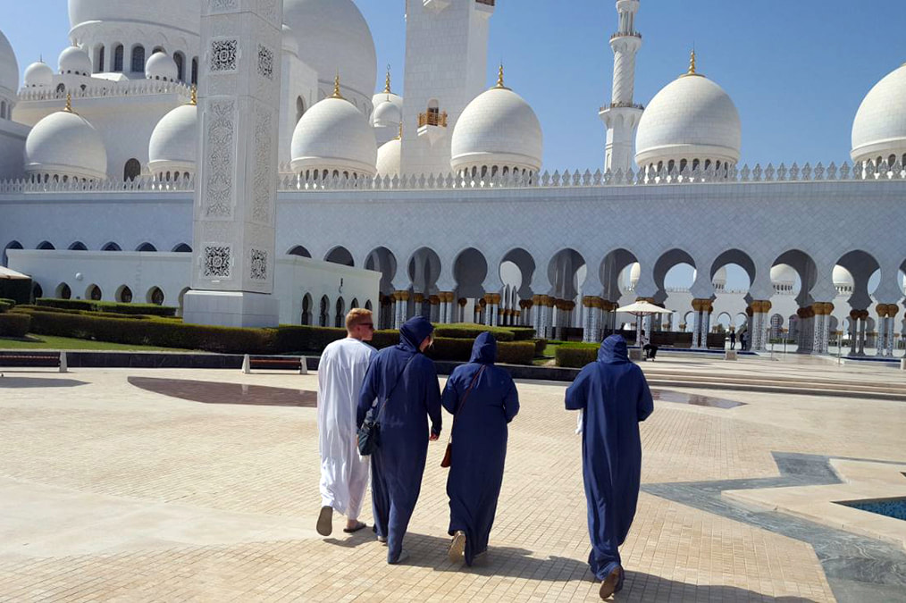 Picture of a man and three woman wearing traditional long robes, walking towards the Sheikh Zayed Mosque in Abu Dhabi 