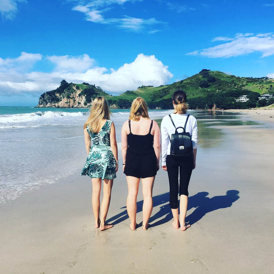 Three woman standing on the beach facing away from the camera overlooking the ocean and peninsula 