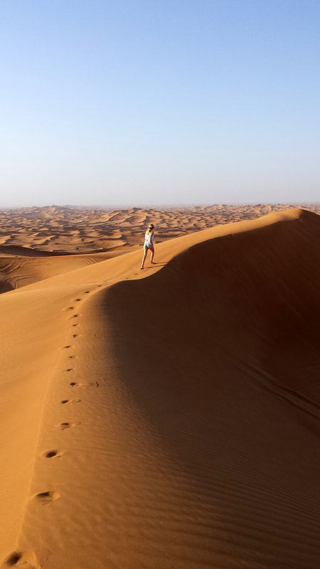 Picture of a woman walking up a sand dune in the Dubai desert 