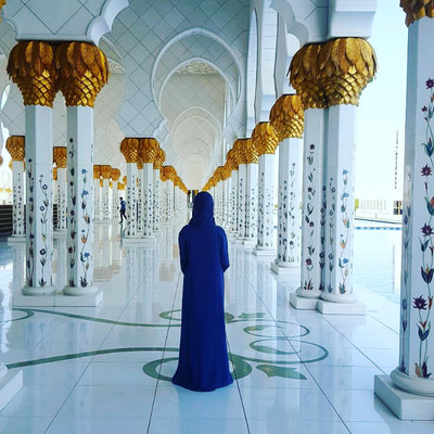 Woman stands in blue robe looking out at ornate mosque