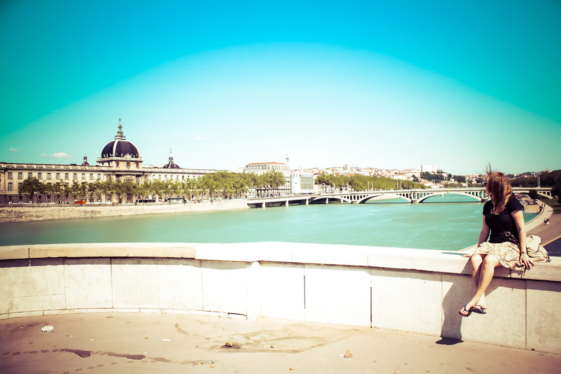 Picture of a woman sitting on a bridge looking at the river Seine and skyline of Paris 