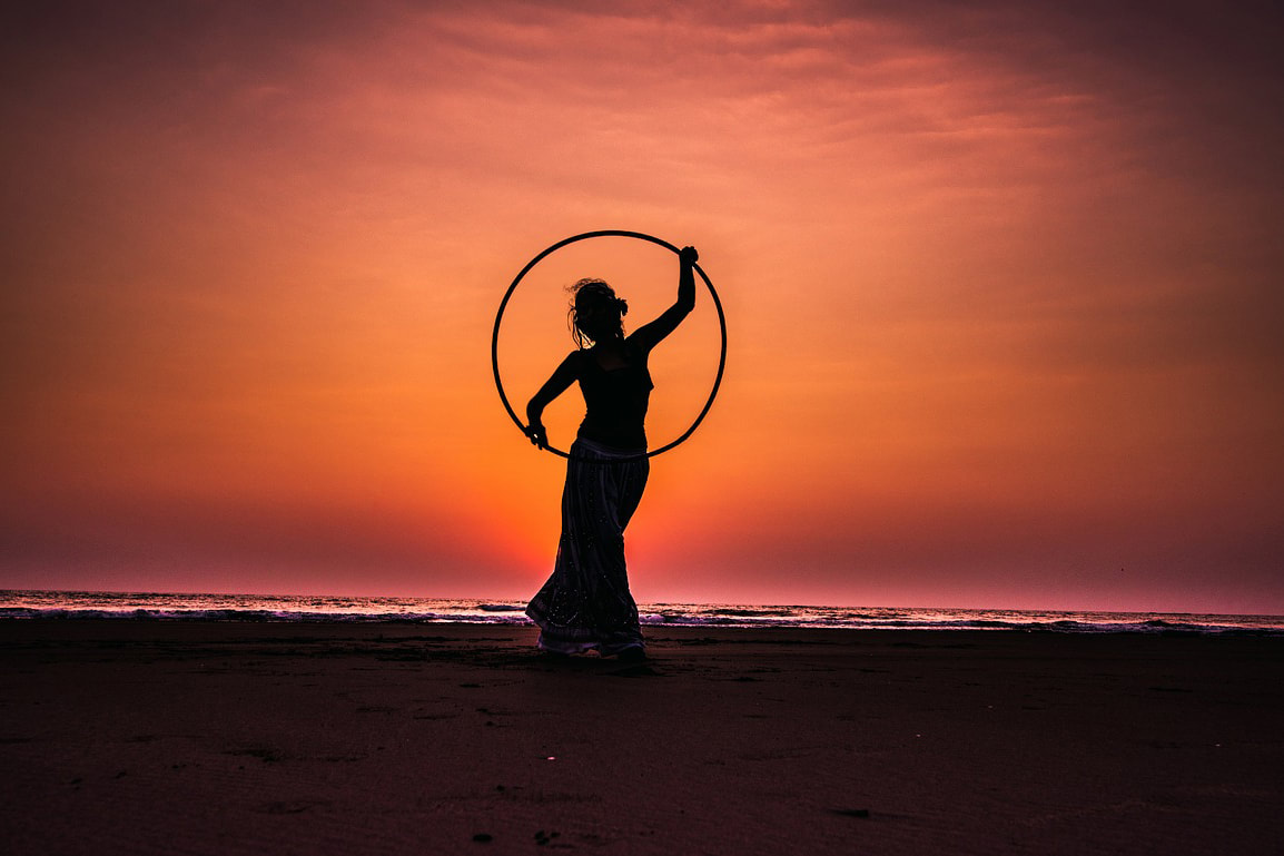Girl holding a hula hooping on the beach at sunset