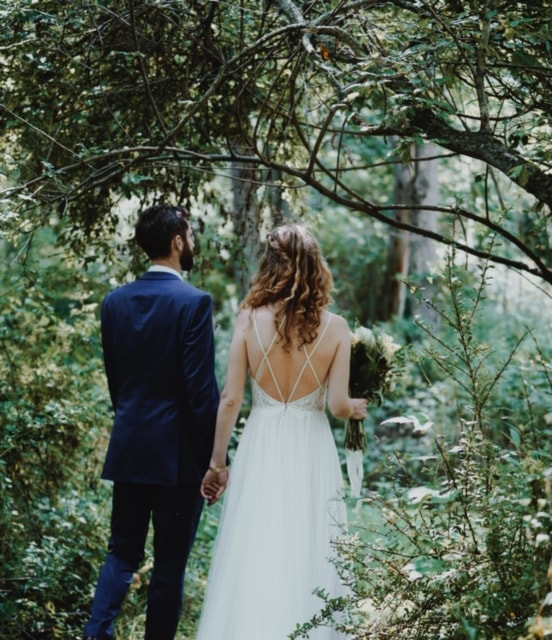 A couple on their wedding day standing among trees facing away from the camera and holding hands