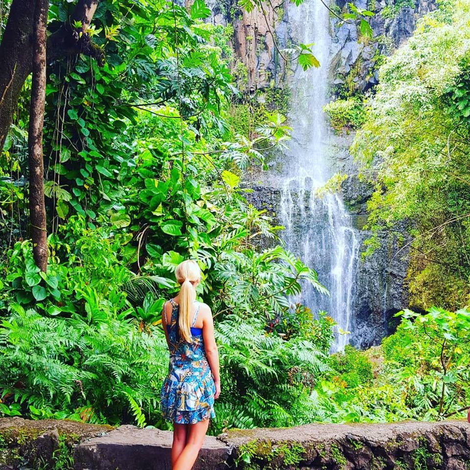 Picture of a woman standing in front of a waterfall surrounded by rain forest in Hawaii