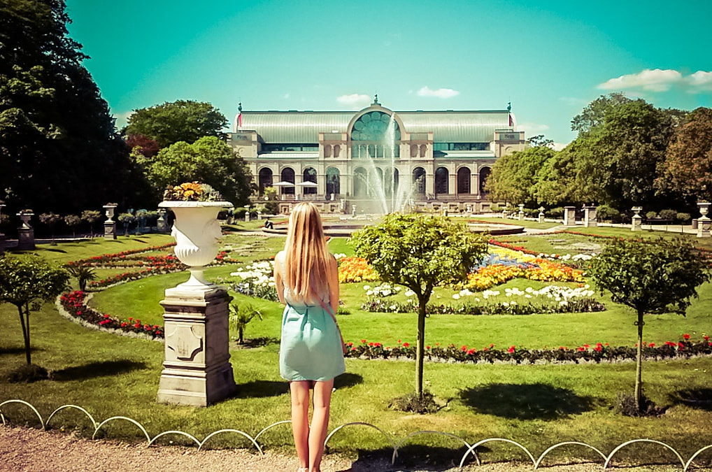 Woman standing in front of a garden with museum building in the background, facing away from the camera at  the flora in Cologne, Germany. 