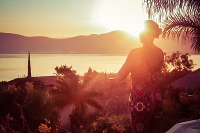 Woman standing in the setting sun, overlooking a tropical setting