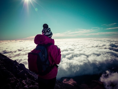 Woman standing on top of Mount Taranaki in NZ overlooking clouds