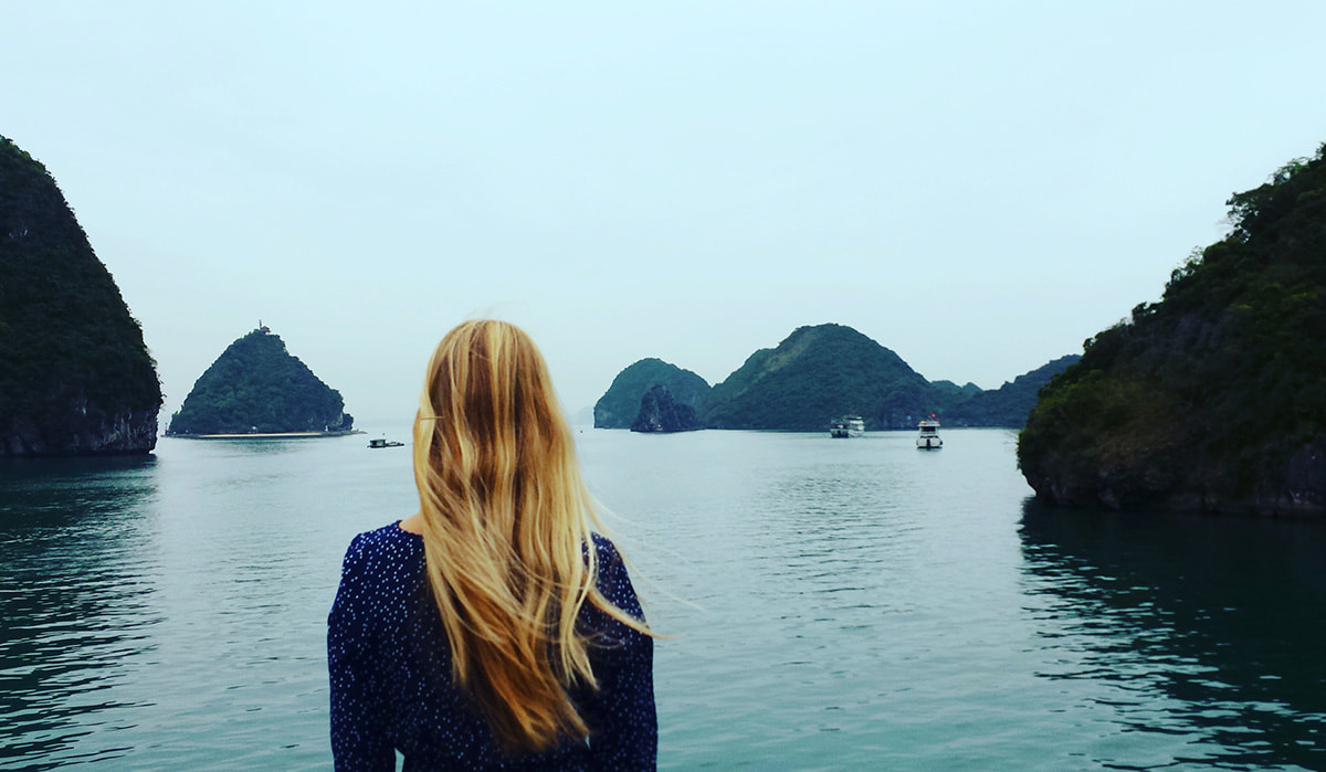 A woman looks out at Halong Bay as her boat glides along the bay