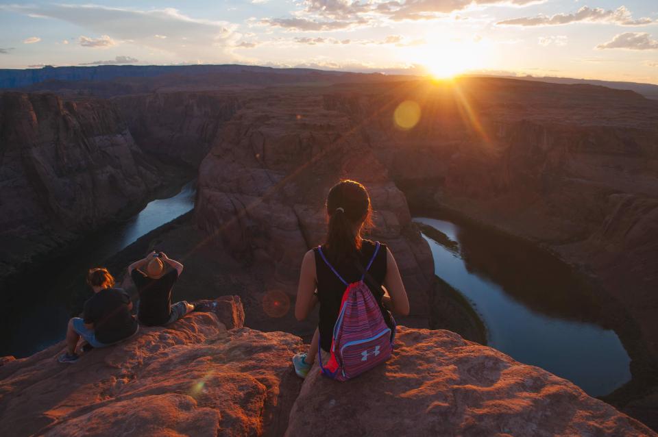 Woman with a backpack overlooks water-filled canyon with sun setting in the distance