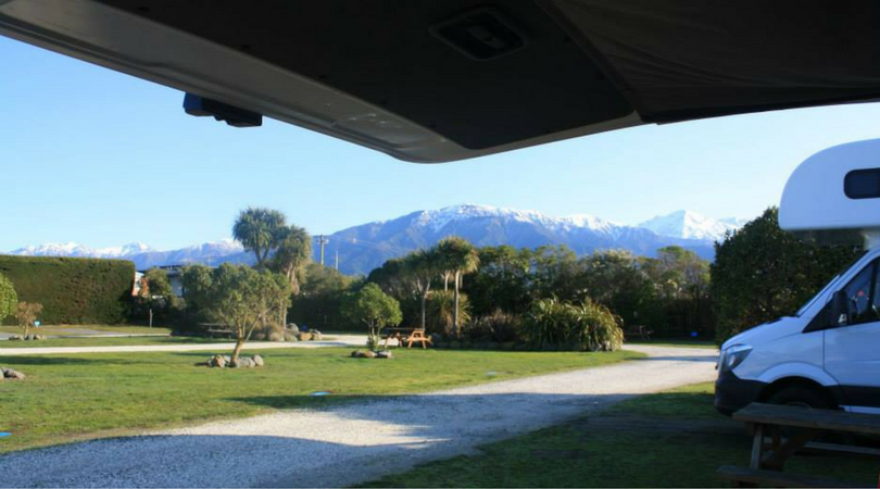 A motorhome sits in a South Island campground with mountains in the distance