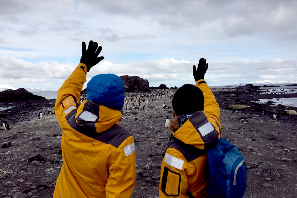 Picture of two people waving at penguins on an island in Antarctica 