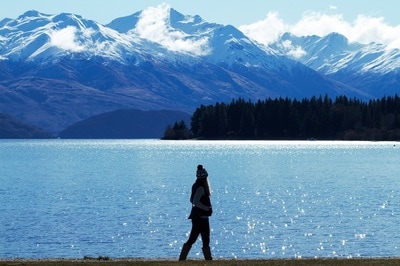 A woman stands in front of lake and mountain backdrop in Wanaka, NZ